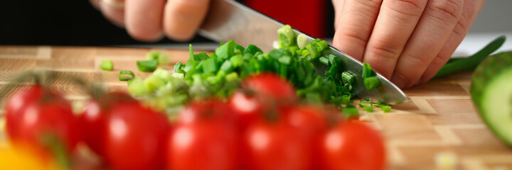 Close up of man cutting green fresh onion for salad in the kitchen at home. Cooking recipes concept