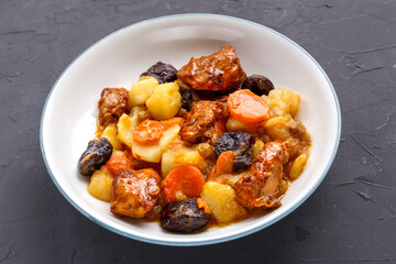 A dish of Jewish cuisine sweet tsimes with carrots, dates and turkey meat in a white plate on a concrete background.