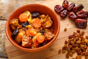 Jewish cuisine dish sweet zimmes with dates, carrots and turkey meat in a brown plate on a black board