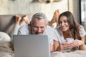 Couple staying in the bed with coffee and computer