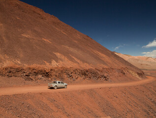 Adventure and explore in the arid desert. View of a 4x4 pickup truck driving along the extreme dirt road across the red Andes mountains and dunes in La Rioja, Argentina. © Gonzalo