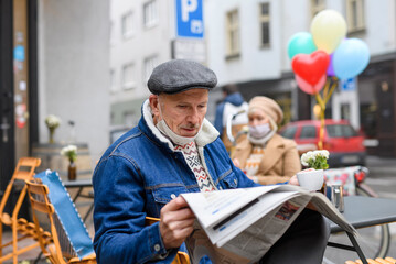 Senior people sitting and reading newspapers in outdoor cafe in city, coronavirus concept.