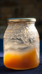 Restos de miel en bote de cristal con tapa metálica dorada junto a ventana de madera y cortina...