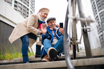 Happy senior couple outdoors on sidewalk in city, taking selfie.