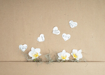 brown paper background with paper hearts and small white orchid blossoms with moss for greeting card or sign