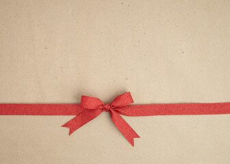 Brown kraft paper background for text, invitations, signs or holiday greetings with red fabric ribbon from above