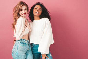 Two young beautiful smiling international hipster female in trendy summer jeans clothes. Sexy carefree women posing near pink wall in studio. Positive models having fun. Concept of friendship