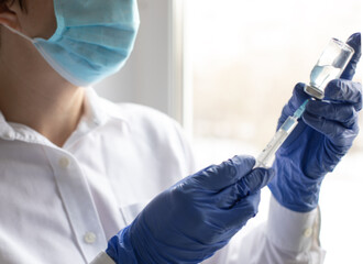 Female hands in blue medical gloves hold a syringe and a bottle of medicine or vaccine