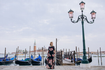 A girl walks along the pier against the backdrop of blue gondolas. A tourist travels around Venice.