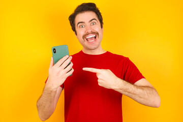 Young Caucasian man wearing red t-shirt standing against yellow background holding in hands showing new cell,