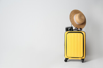 Travel suitcase with hat, camera and sunglasses on light grey background, space for text. Summer vacation