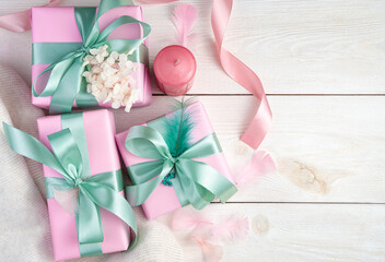 Three pink gift boxes, a candle and ribbons on a white wooden background. Top view, with space to copy. The concept of festive backgrounds, March 8.
