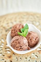 Chocolate ice cream with mint leafe. three balls in a white bowl on a vintage table.