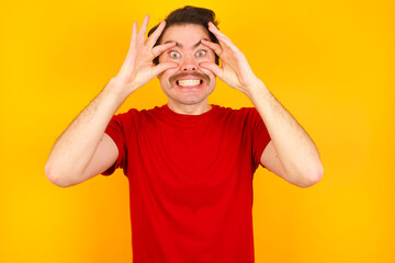 Fototapeta na wymiar Young Caucasian man wearing red t-shirt standing against yellow background keeping eyes opened to find a success opportunity.