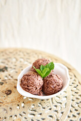 Chocolate ice cream with mint leafe. three balls in a white bowl on a vintage table.