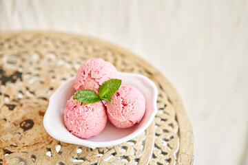 Strawberry ice cream with mint leaf. three balls in a white bowl on a vintage table. sorbet