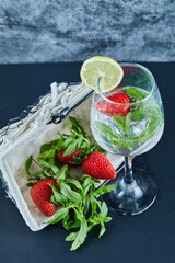 A glass of juice with whole fruits inside and basket of strawberries on blue background