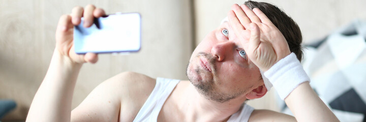 Obraz premium Adult funny man doing sports at home and recording on his mobile phone while holding in hands. Health and sport concept