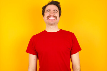Young Caucasian man wearing red t-shirt standing against yellow background very happy and excited...