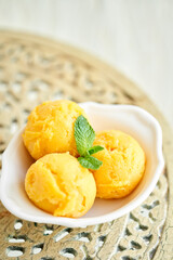 Mango ice cream with mint leaf. three balls in a white bowl on a vintage table. sorbet