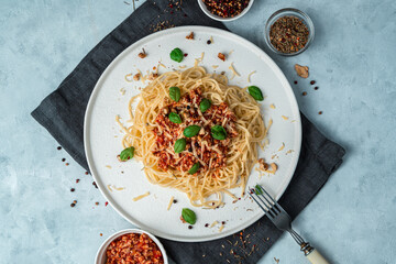 Pasta and tomato sauce with minced meat, basil, cheese and nuts in a flat plate on a gray background. Top view, horizontal orientation. Culinary background.