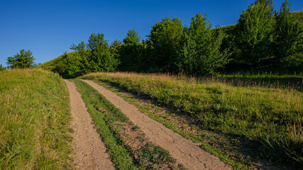 Fototapeta na wymiar Dirt road at the foot of a hill, panoramic rural landscape.