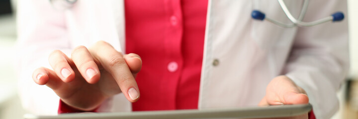 Close up of female physician standing with stethoscope and using digital tablet while typing in the office. Health and care concept