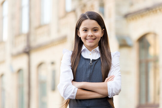 Confident happy kid smile in school uniform keeping arms crossed outdoors, confidence