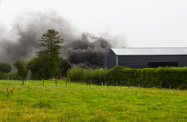 Fototapeta na wymiar Hazardous toxic thick black smoke from burning rubber tyres on a farm in County Tyrone in Northern Ireland