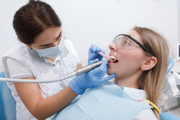 Professional dentist working at her clinic, treating teeth of female patient