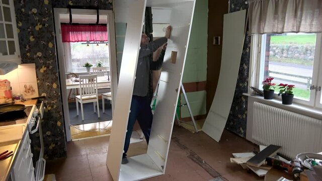 A man breaks kitchen cabinet during kitchen renovation. The kitchen cabinet falls apart and the man is doubtful about his abilities.