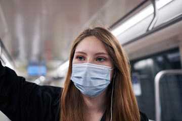 Fototapeta na wymiar ¡A beautiful white Latina woman using the city subway leaning on a support with her right hand wearing a mask for the coronavirus pandemic close up