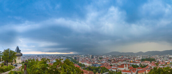 Cityscape of Graz and the clock tower (Grazer Uhrturm), famous tourist attraction on Shlossberg hill, Graz, Styria region, Austria, at sunset. Dramatic sky, panoramic view