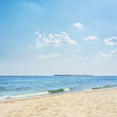 Fototapeta premium Blue sea and yellow sand and an island on the horizon with blue skies and white clouds above it.