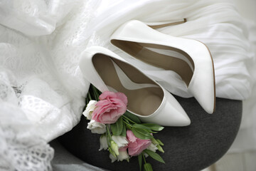 Pair of white high heel shoes, flowers and wedding dress on chair, above view