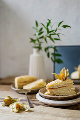Two pieces of cake Napoleon on a plate, wooden rustic table with mirror and flower vase. Russian...