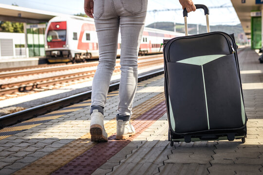 Tourist pulling large heavy luggage. Woman with suitcase walking at railroad station platform. Travel to vacation by train
