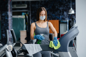 Fototapeta na wymiar The girl in the mask disinfecting the gym equipment during a pandemic.