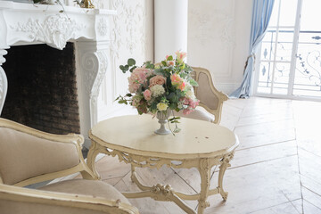 luxurious light interior in the Baroque style. A spacious room with a road chic beautiful furniture, a fireplace and flowers. plant stucco on the walls and light wood parquet