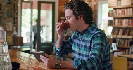 Young men sitting at counter in cafe bookstore looking at tablet 