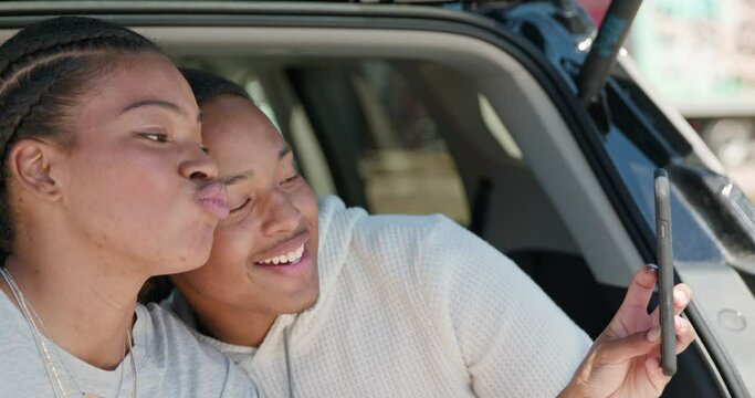 Young African American couple having impromptu picnic lunch in the back of their vehicle, taking selfie with mobile phone 