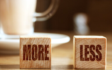 Wooden blocks on wooden table with More and Less signs. business concept