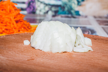 Sliced vegetables for cooking. Vegetables on a round wooden cutting board lying on the kitchen table. Chopped onion.