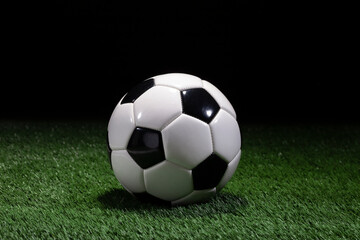 Fototapeta na wymiar Traditional black and white soccer ball on green field with dark background