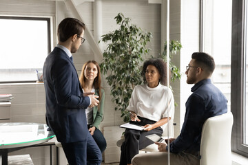 Diverse colleagues sitting in circle, listening to team leader at meeting, mentor coach giving...