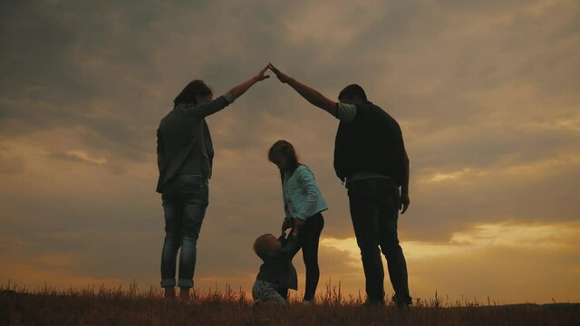 Silhouette of happy family with dream house. Family parents making home for kids at sunset, secure and protecting home. Concept of friendly family.