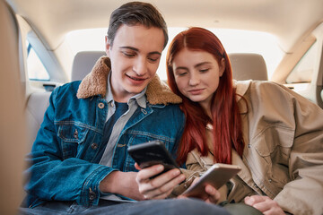 A couple of teenagers using their smartphones while sitting on back seat in the car