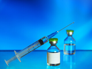 drop of transparent vaccine on the tip of a needle syringe, glass vials, blue background, a horizontal image with a soft focus, a wide banner, a place for text