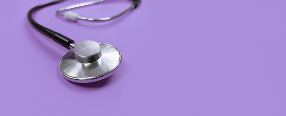 Black stethoscope on purple background with copy space.