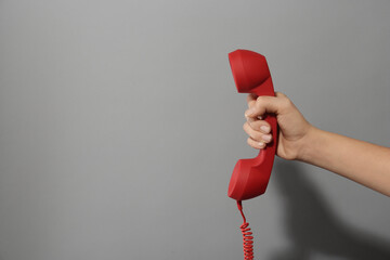 Closeup view of woman holding red corded telephone handset on light grey background, space for text. Hotline concept